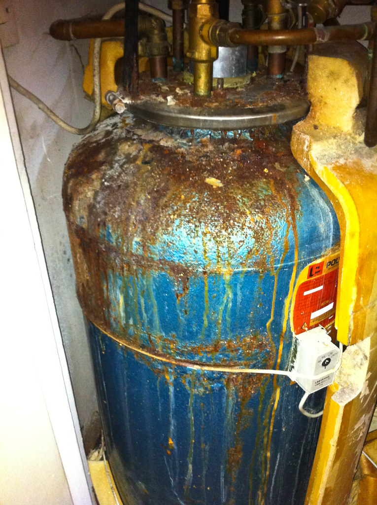 An older hot-water cylinder showing surface corrosion and staining around its fittings — the kind of condition to photograph and report.