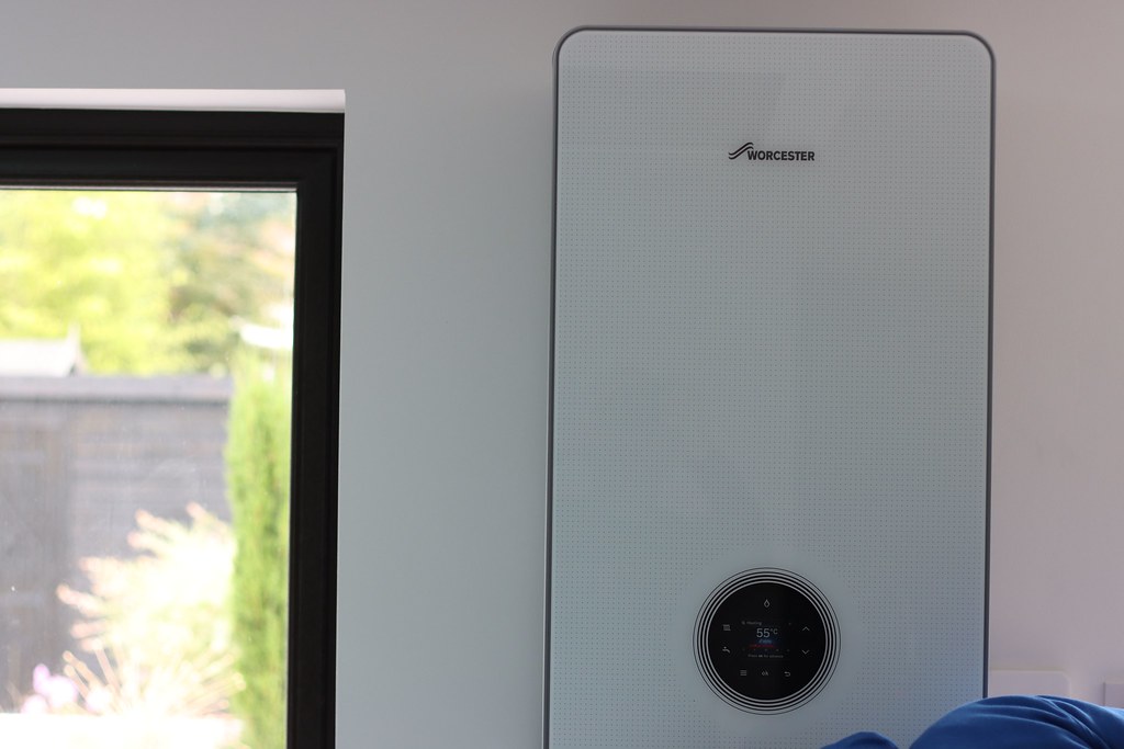 A white wall-hung combination boiler mounted above kitchen units, with pipework running down into the cupboard below and no hot-water cylinder in view.